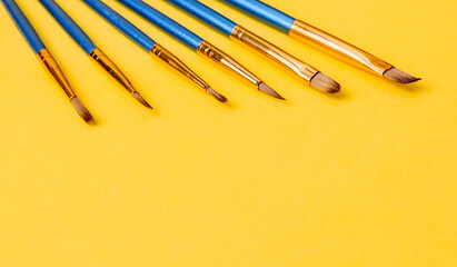 set of brushes on yellow.

Set of blue brushes on a yellow paper background, close-up side view.