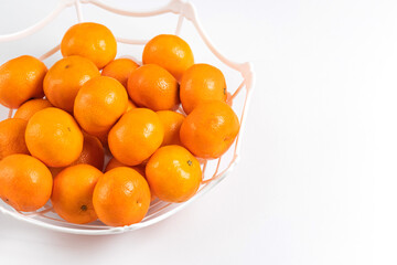 Ripe citrus fruits: tangerines, mandarins, clementines in white basket over white background. Space fot text.
