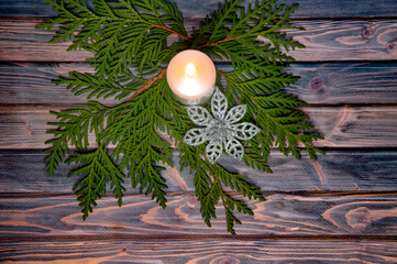 Christmas branches of pine needles and a candle on a dark wooden background.