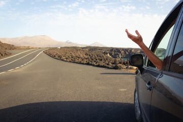 Arm of woman coming out of car window parked on side of road in Lanzarote volcanic island. Summer vacation, car rental, travel journey concepts