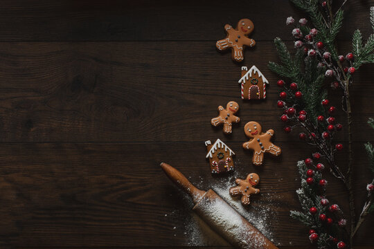 Christmas or New Year background with gingerbread cookies, gingerbread man, gingerbread house, lour  and fir tree branch on dark wood background. Copy space for text, table top view.