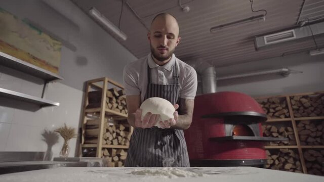 Slow motion. The baker throws the dough on the table with flour.	