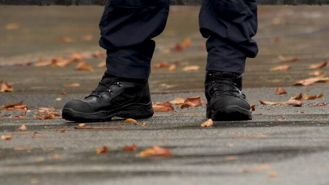 Autumn. Details. Military boots on the man's feet. Policeman's feet. Boots of Police officer in uniform. Legs of a policeman close up on duty. Feet of security guard in black boots. Fallen Leaves