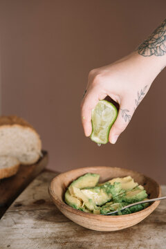 Woman hand squeezing lime in avocado salad kept on cutting board at kitchen