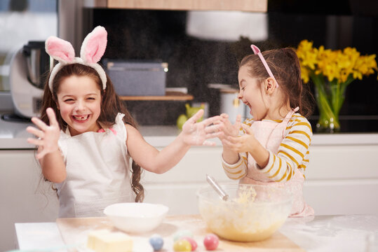 Two playful sisters having fun baking Easter cookies in kitchen together