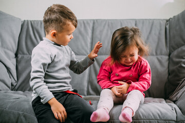 The older brother scolds his little sister sitting on the couch