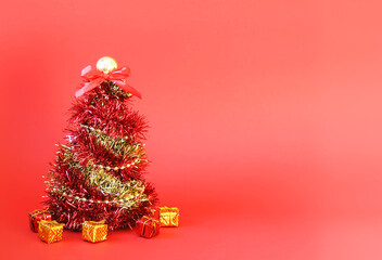 Christmas tree made of shiny bright decorative garland and gift boxes on red background