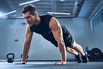 Athletic man doing pushups exercise at gym
