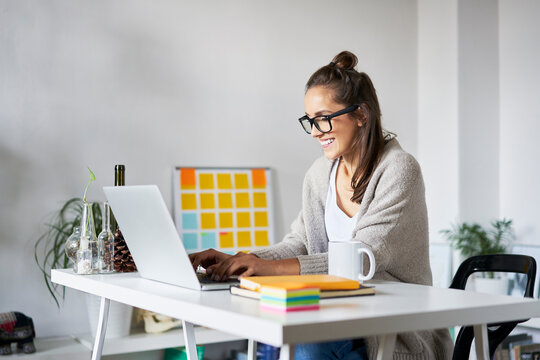 Smiling Young Woman At Home Using Laptop On Desk