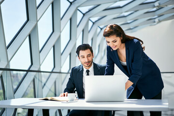 Smiling businesswoman and businessman using laptop at desk in modern office