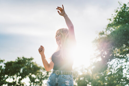 Back lit beautiful young woman dancing against sky