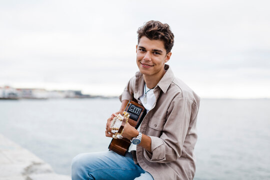Smiling man playing guitar while practicing at promenade against sky