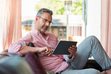 Mature man sitting on couch at home using a tablet