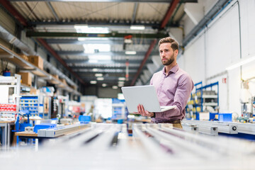 Young businessman using laptop in production hall