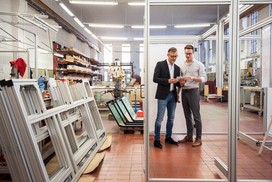 Two businessmen in factory looking at tablet