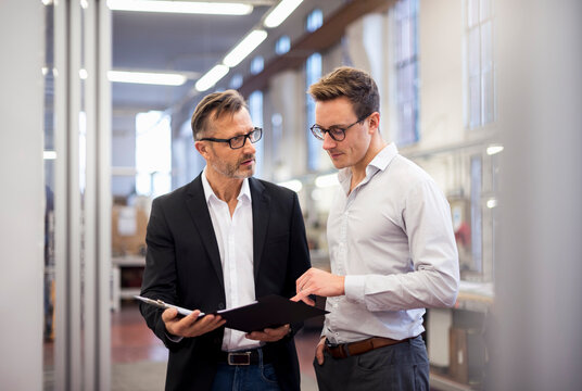 Two businessmen in factory looking at folder