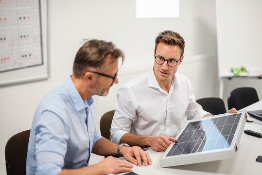 Two businessmen examining solar panel on desk in office