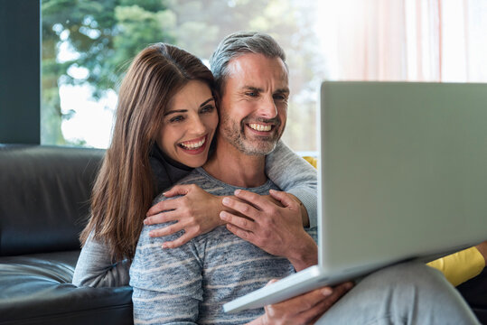 Happy couple on couch at home sharing a laptop