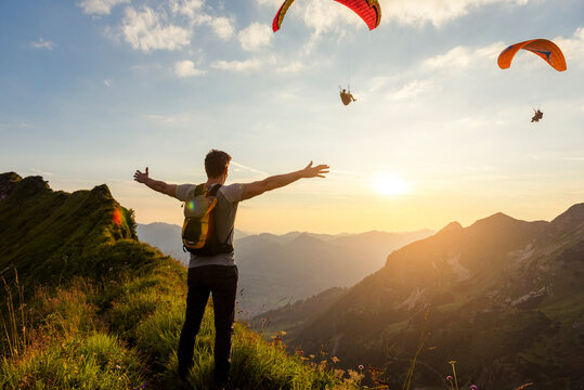 Germany, Bavaria, Oberstdorf, man on a hike in the mountains at sunset with paraglider in background