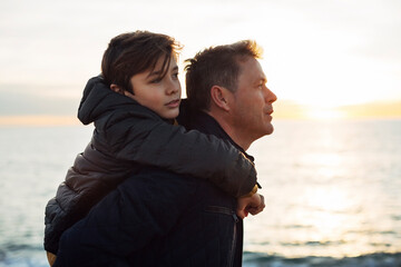 Father carrying son piggyback by the sea