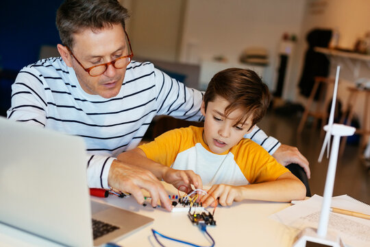 Father and son assembling a construction kit with laptop and wind turbine model