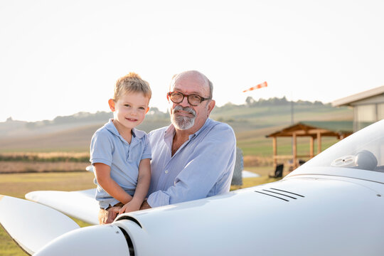 Grandfather picking up grandson while standing at airfield on sunny day