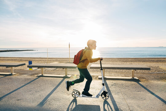 Boy riding scooter on beach promenade at sunset
