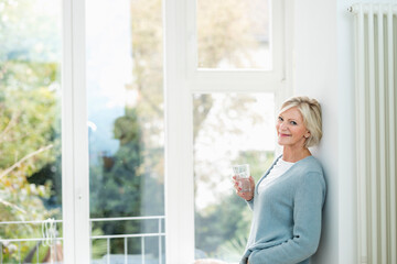 Portrait of senior woman with glass of water in front of window