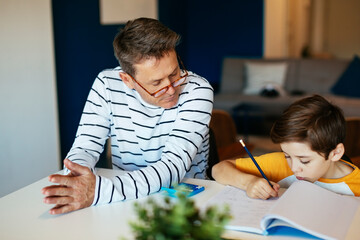 Father watching son doing homework at table