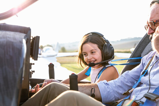 Young little girl inside aircraft cockpit with grandfather at airfield on sunny day