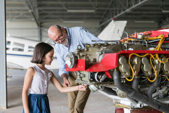 Grandfather showing how to fix airplane tool to granddaughter while standing in hangar