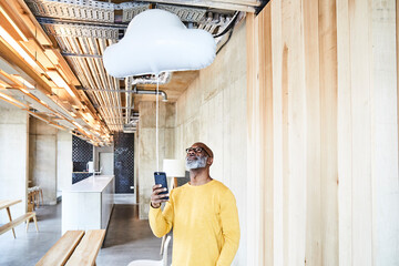 Mature businessman holding cell phone attached to cloud balloon