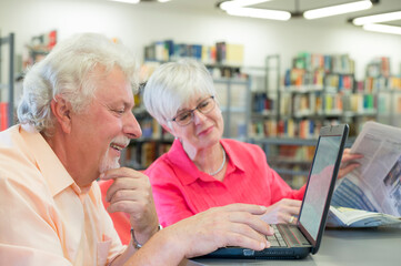 Senior couple with laptop and newspaper in a city library