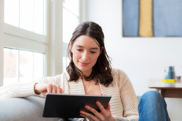 Woman sitting on couch at home using tablet