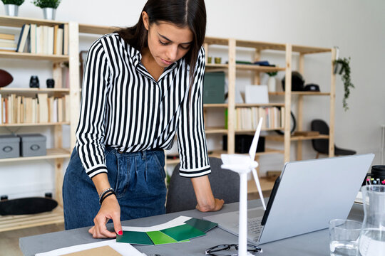 Young female architect making decision in choosing color shade from swatches at desk in office