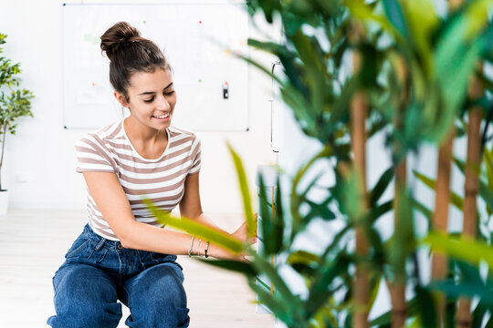 Smiling beautiful female design professional crouching by rack at creative office