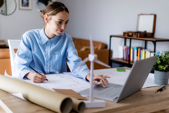 Woman in office working on plan and laptop with wind turbine model on table