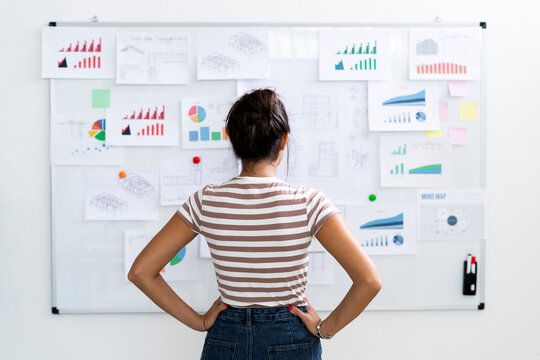 Young female architect with hands on hip examining charts on whiteboard at office