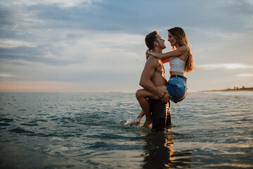Man carrying woman while standing in water during sunset at beach