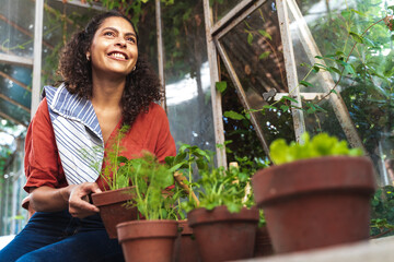 Mature woman smiling while looking away holding plant sitting in garden shed