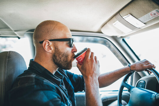 Young man with sunglasses and beard on a road trip with takeaway drink
