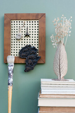 DIY picture frame with wicker rack holding various mementos, stack of books, paintbrush and vase with dried plants