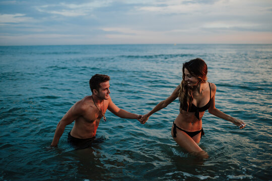 Couple holding hand while walking in water at beach during sunset