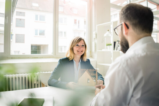 Woman with house model smiling at man in office