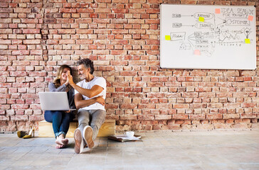 Businessman and woman sitting in a loft, giving high five, founding a start-up company