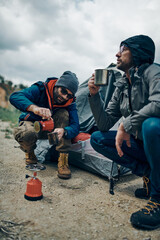 Two explorers crouching next to the tent and drinking coffee.