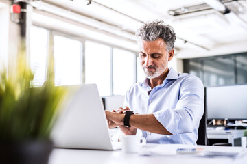 Mature businessman sitting at desk in office looking at smartwatch
