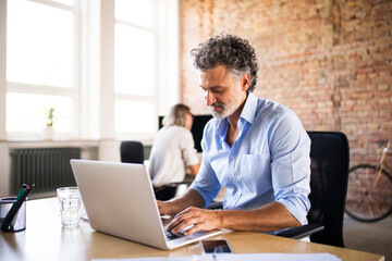Businessman using laptop in office with colleague in background