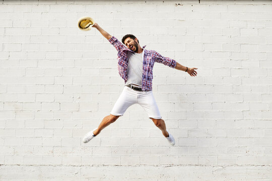 Happy man jumping mid-air in front of white wall