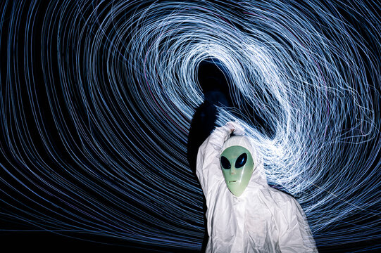 Man in alien costume standing under light trails at night